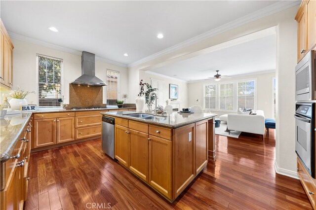 kitchen featuring sink, a kitchen island with sink, stainless steel appliances, light stone countertops, and wall chimney range hood