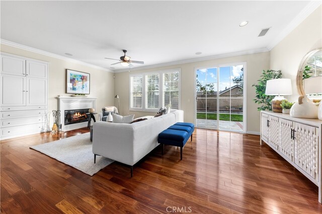 living room with ornamental molding, dark wood-type flooring, and ceiling fan