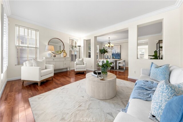 living room with dark wood-type flooring, ornamental molding, and a chandelier