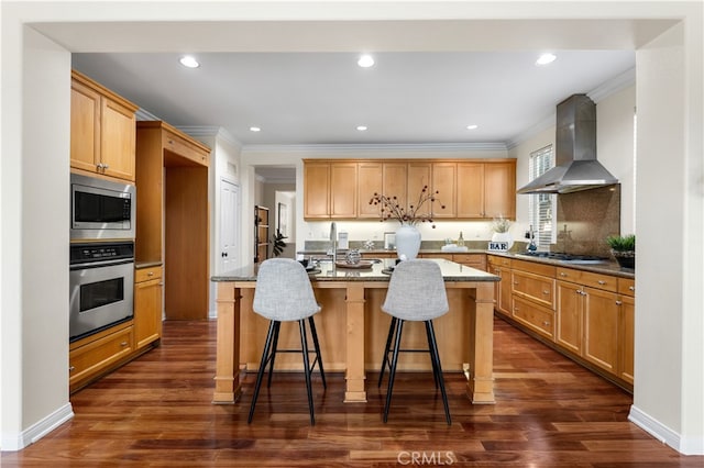 kitchen featuring a breakfast bar area, a center island with sink, appliances with stainless steel finishes, light stone countertops, and wall chimney range hood