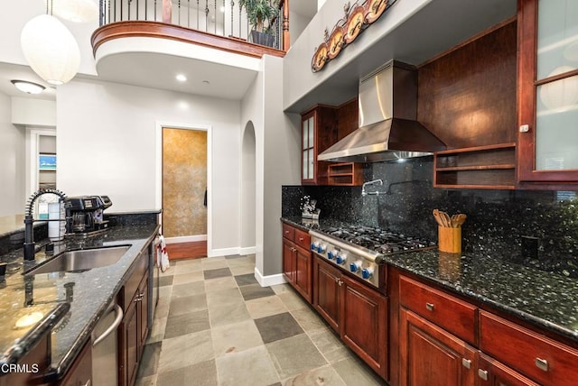 kitchen with pendant lighting, wall chimney range hood, sink, stainless steel appliances, and dark stone counters