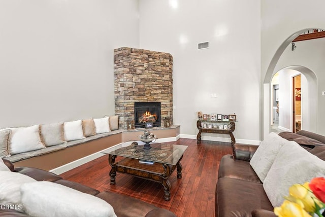 living room with dark hardwood / wood-style flooring, a stone fireplace, and a high ceiling