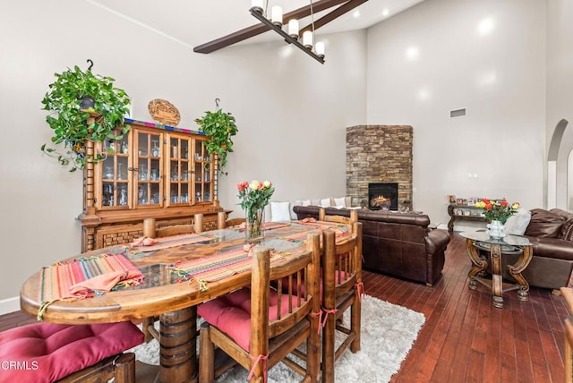 dining room with dark wood-type flooring, a towering ceiling, a fireplace, and an inviting chandelier