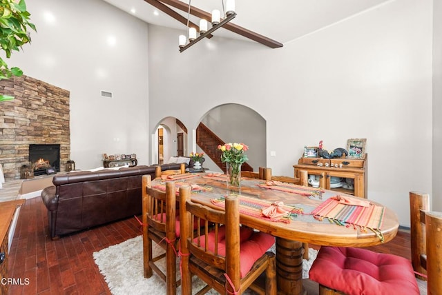 dining area with a towering ceiling, a chandelier, a fireplace, and dark hardwood / wood-style flooring