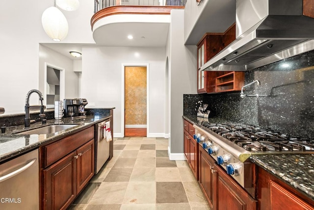 kitchen featuring sink, decorative light fixtures, dark stone countertops, stainless steel appliances, and wall chimney range hood