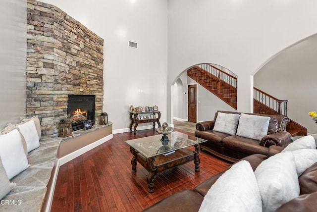 living room with hardwood / wood-style flooring, a stone fireplace, and a towering ceiling