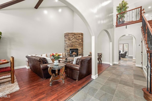 living room with beamed ceiling, a towering ceiling, a stone fireplace, and hardwood / wood-style floors