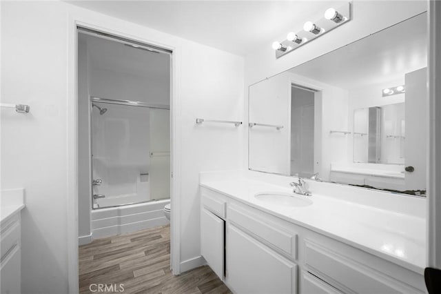 full bathroom with hardwood / wood-style flooring, vanity, toilet, and combined bath / shower with glass door