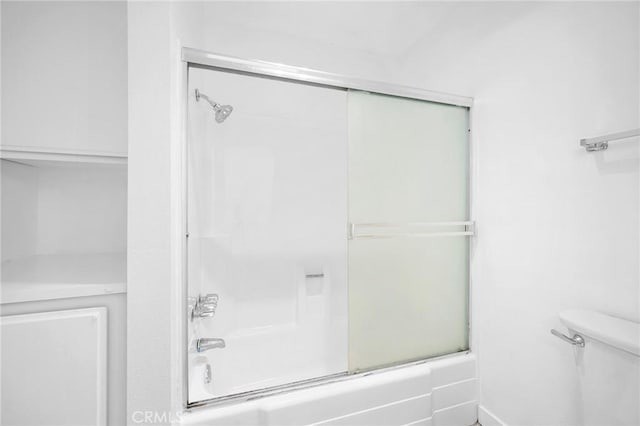 bathroom featuring toilet and bath / shower combo with glass door