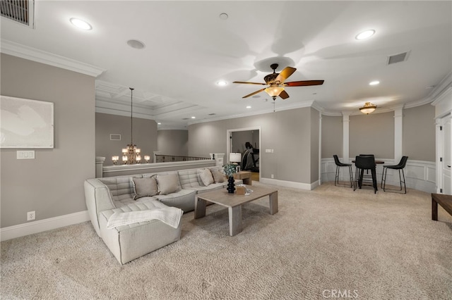 carpeted living room with decorative columns, crown molding, and ceiling fan with notable chandelier