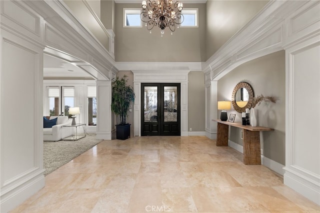 entryway with french doors, a towering ceiling, ornamental molding, and a chandelier