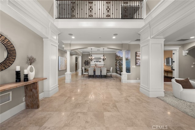 entrance foyer featuring a towering ceiling, ornamental molding, a chandelier, and decorative columns