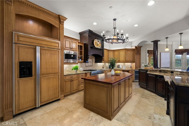 kitchen featuring a center island, built in appliances, wooden counters, and decorative light fixtures