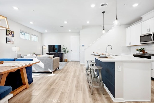 kitchen featuring sink, white cabinetry, light hardwood / wood-style flooring, pendant lighting, and decorative backsplash