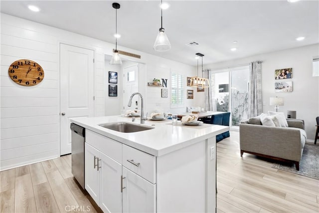 kitchen featuring pendant lighting, white cabinetry, sink, stainless steel dishwasher, and a center island with sink