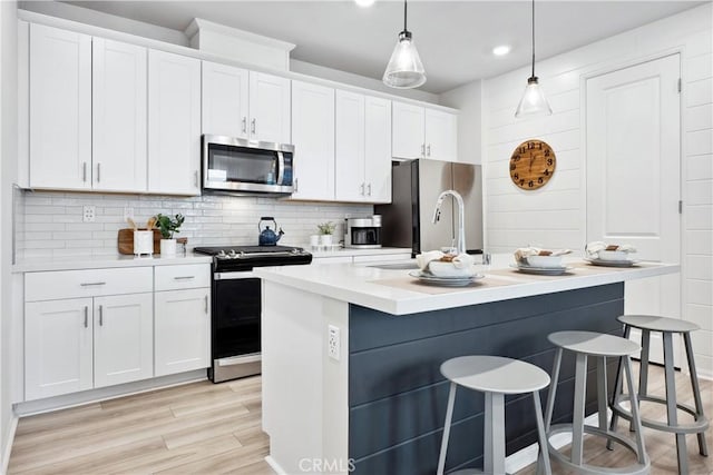 kitchen with white cabinets, backsplash, hanging light fixtures, a kitchen island with sink, and stainless steel appliances