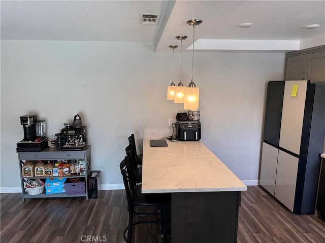 kitchen with hanging light fixtures, dark wood-type flooring, fridge, and a kitchen bar