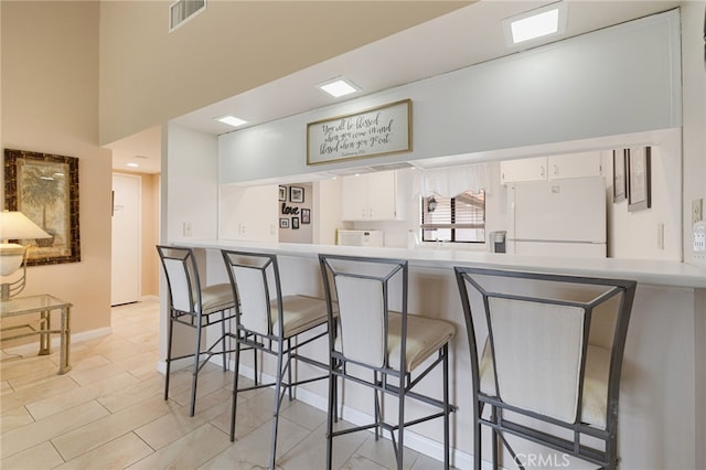 kitchen featuring white cabinetry, a breakfast bar area, kitchen peninsula, and white fridge