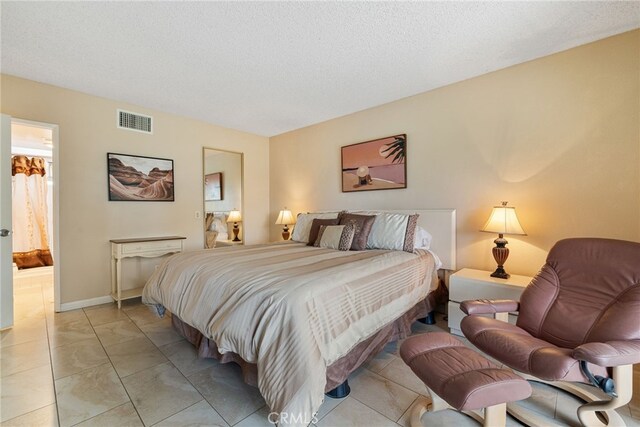 bedroom with connected bathroom, a textured ceiling, and light tile patterned flooring