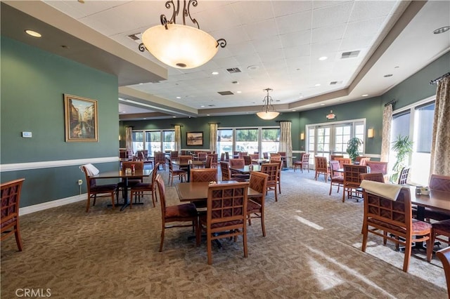 carpeted dining space with a raised ceiling, visible vents, baseboards, and french doors