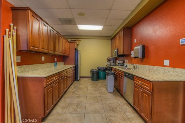 kitchen with light tile patterned floors, brown cabinets, stainless steel appliances, a paneled ceiling, and a sink