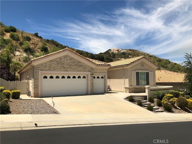 mediterranean / spanish-style house featuring a garage, concrete driveway, stone siding, a tile roof, and a mountain view