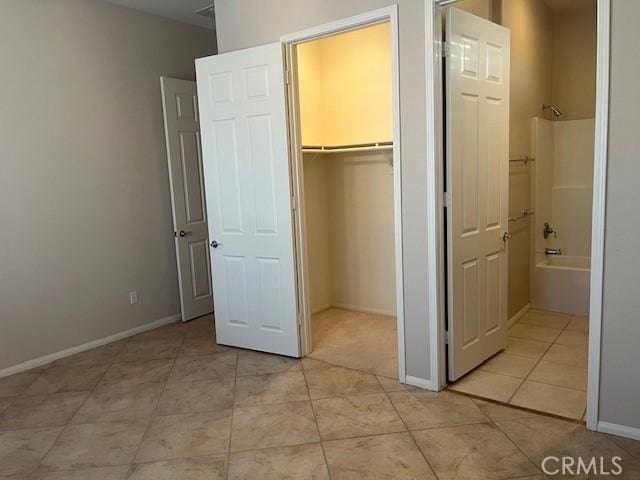 unfurnished bedroom featuring baseboards, ensuite bathroom, a spacious closet, a closet, and light tile patterned flooring