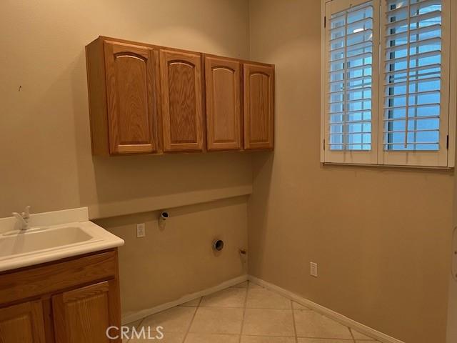 washroom with cabinet space, a sink, baseboards, and light tile patterned floors