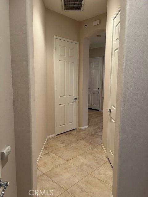 corridor featuring light tile patterned flooring, visible vents, and baseboards