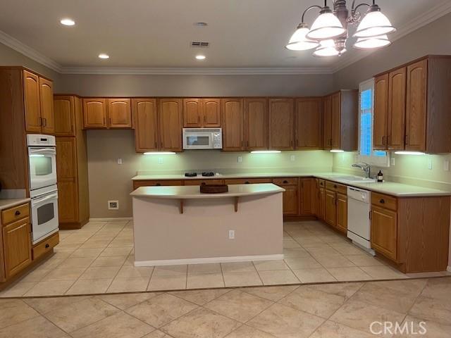 5467 Breckenridge Ave, Banning, CA 92220 - kitchen with white appliances, a chandelier, brown cabinets, a center island, and ornamental molding