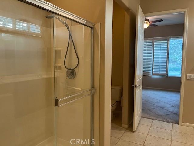 full bath featuring a stall shower, baseboards, a ceiling fan, toilet, and tile patterned floors