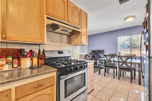 kitchen with light tile patterned flooring, appliances with stainless steel finishes, light brown cabinetry, dark stone counters, and decorative backsplash