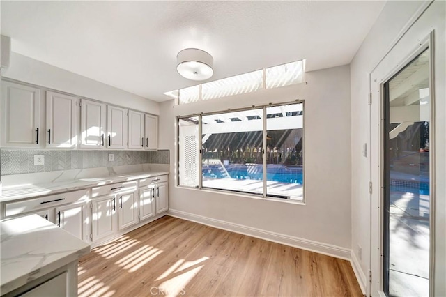 kitchen with white cabinets, light stone countertops, backsplash, and light hardwood / wood-style floors