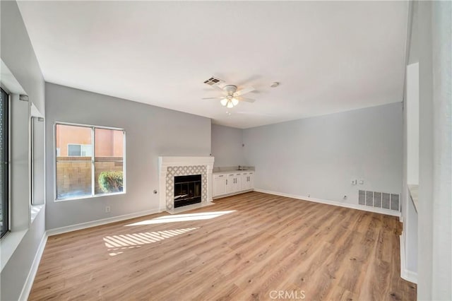 unfurnished living room with a fireplace, ceiling fan, and light wood-type flooring