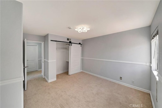 unfurnished bedroom with multiple windows, a barn door, light colored carpet, and a closet