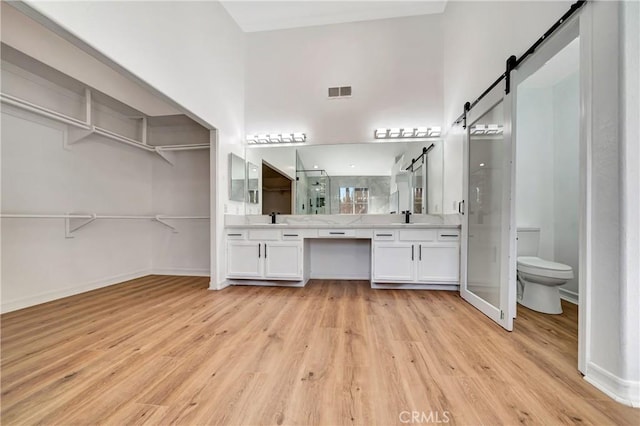 bathroom featuring hardwood / wood-style floors, a high ceiling, vanity, a shower with shower door, and toilet