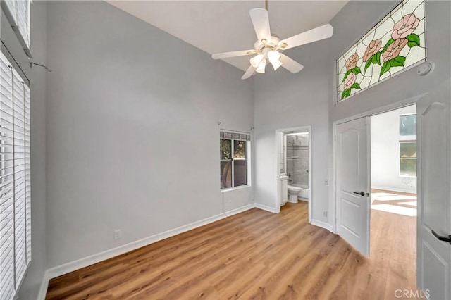 unfurnished bedroom with a high ceiling, ensuite bathroom, ceiling fan, and light hardwood / wood-style flooring