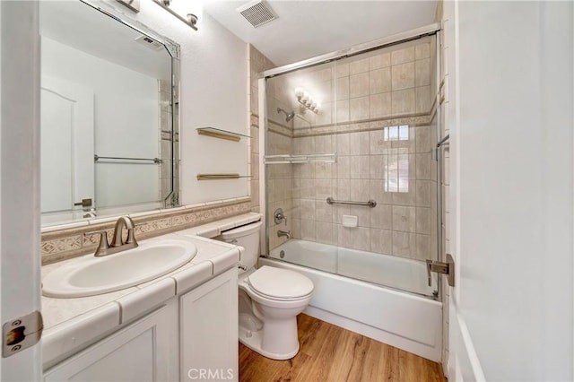 full bathroom with hardwood / wood-style flooring, enclosed tub / shower combo, vanity, and toilet