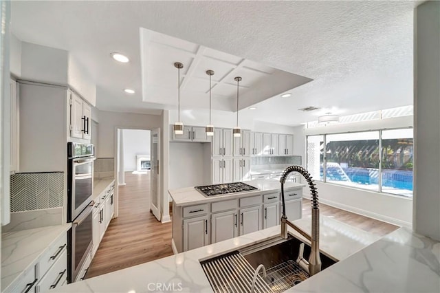 kitchen with hanging light fixtures, white cabinetry, light stone countertops, and stainless steel appliances