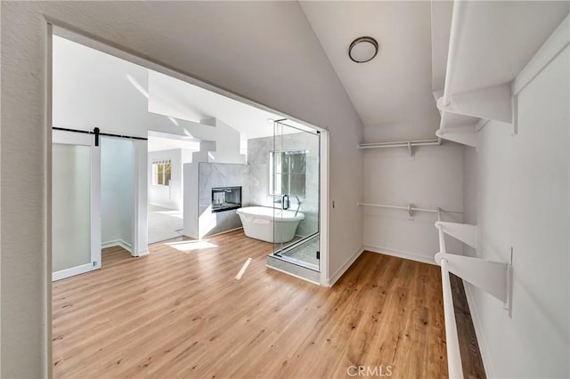 spacious closet with a tile fireplace, vaulted ceiling, a barn door, and light wood-type flooring