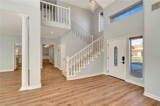 entrance foyer featuring ornate columns, a towering ceiling, and light wood-type flooring