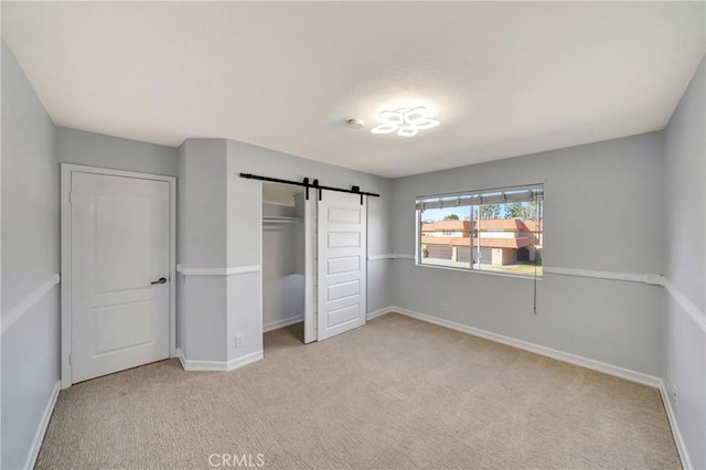 unfurnished bedroom featuring a closet, a barn door, and light carpet