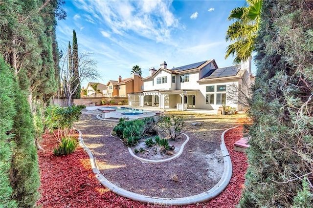 rear view of property featuring a fenced in pool, a patio, and solar panels