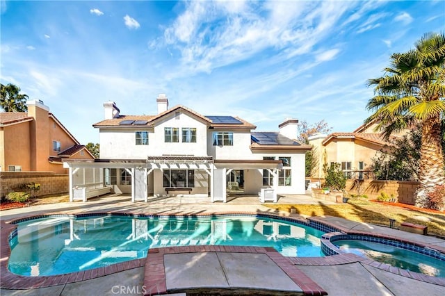 back of property with a pool with hot tub, a patio area, and solar panels