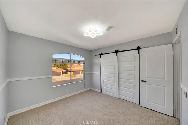 unfurnished bedroom featuring a barn door, light carpet, and a closet