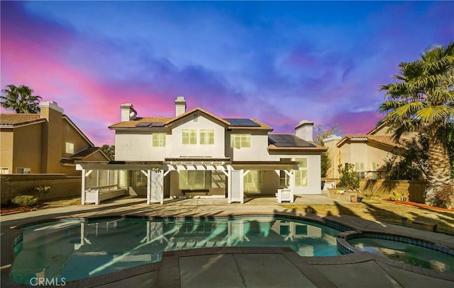 back house at dusk with a swimming pool with hot tub, a pergola, a patio area, and solar panels