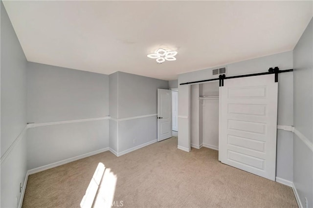 unfurnished bedroom with a barn door, light colored carpet, and a closet