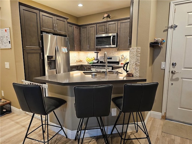 kitchen with dark brown cabinetry, appliances with stainless steel finishes, a kitchen bar, and kitchen peninsula