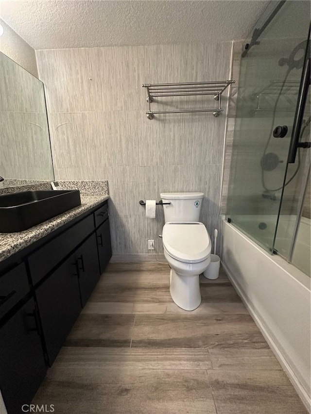 full bathroom featuring toilet, wood-type flooring, a textured ceiling, vanity, and enclosed tub / shower combo