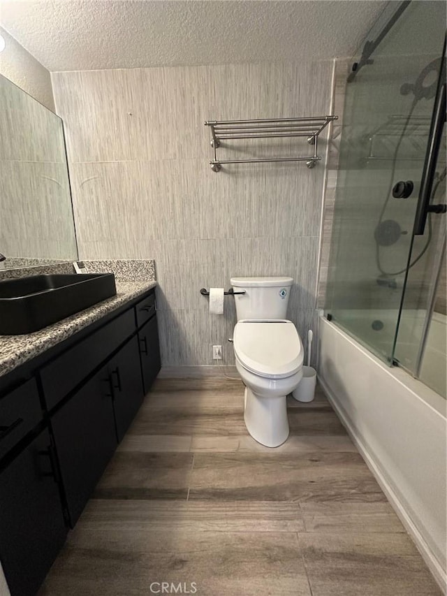 full bathroom with toilet, vanity, wood finished floors, shower / bath combination with glass door, and a textured ceiling